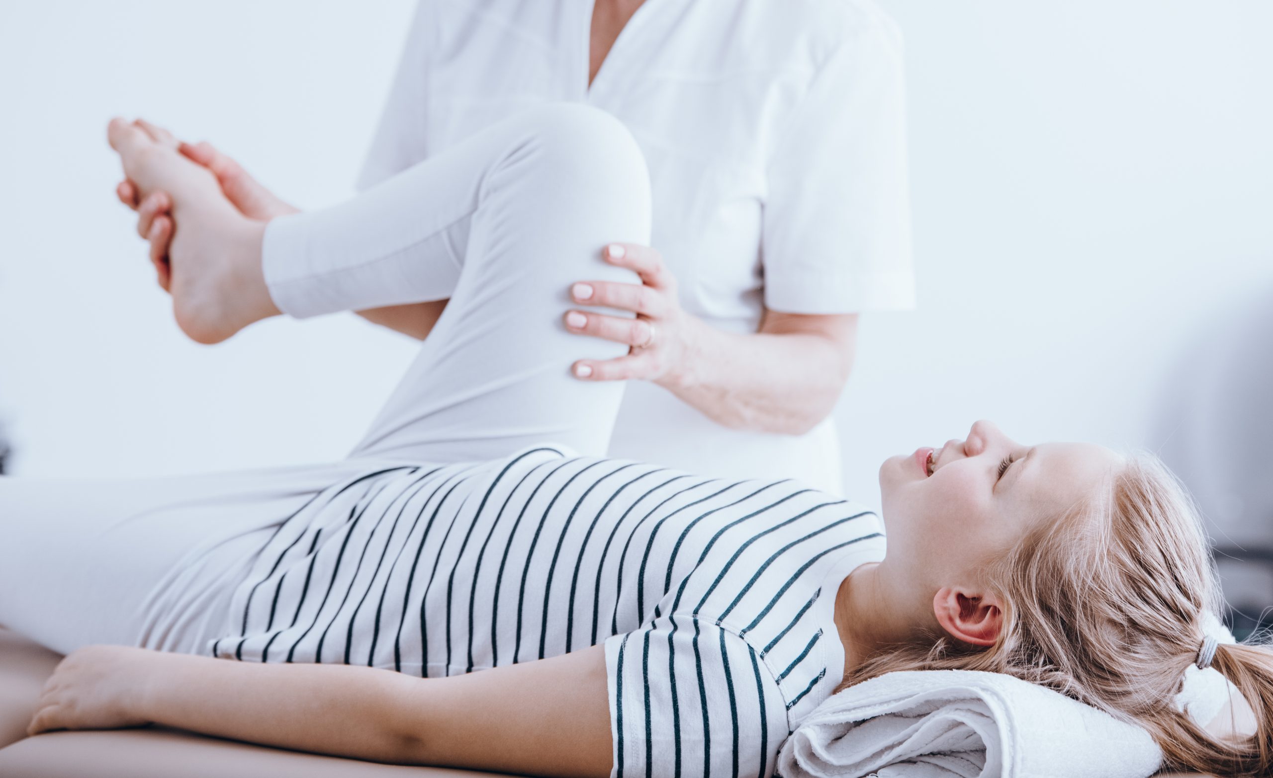 Close-up of happy child stretching her leg during corrective gymnastics with a doctor